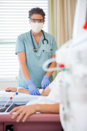 Portrait of mid adult female nurse setting up renal dialysis treatment to patient in hospital room